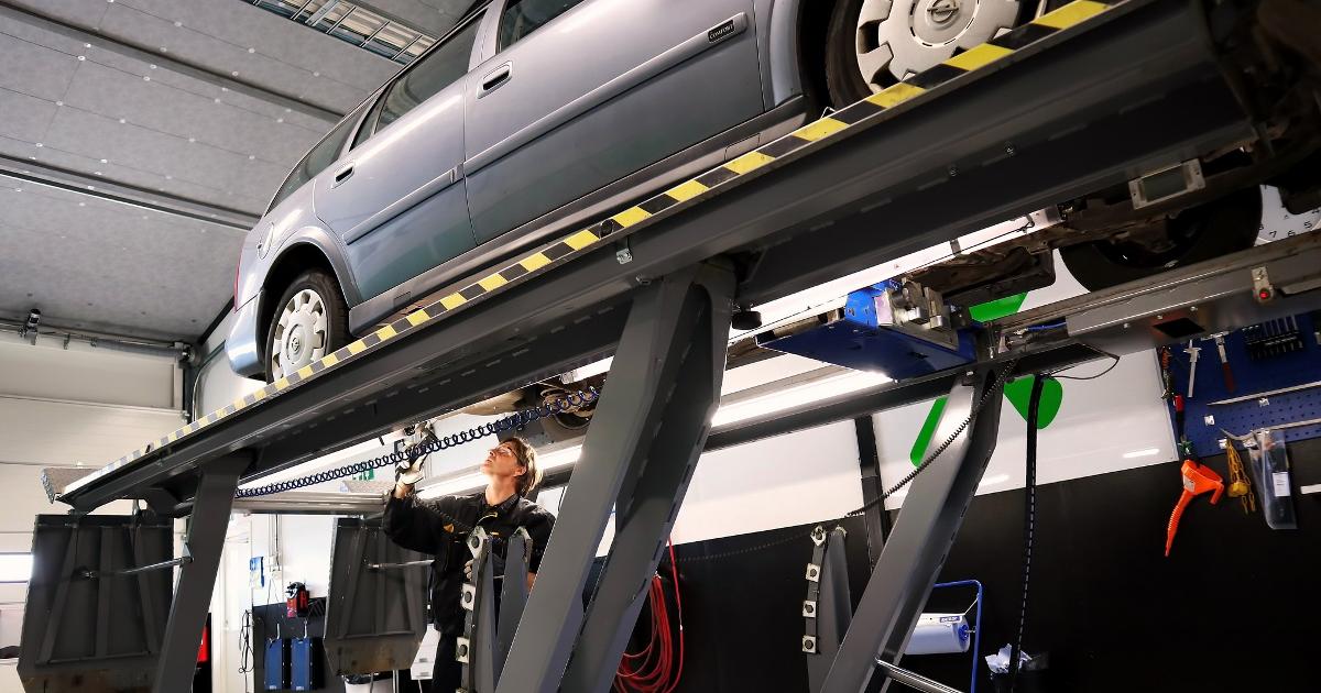 Auto nostettu telineelle katsastusasemalla, katsastusmies tutkii autoa (Kuva: Shutterstock, SariMe)