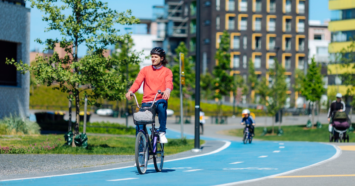 Pyöräilijä kaupungissa, kerrostaloja ja sininen pyörätie. (Kuva: Mika Pakarinen / Keksi Agency)