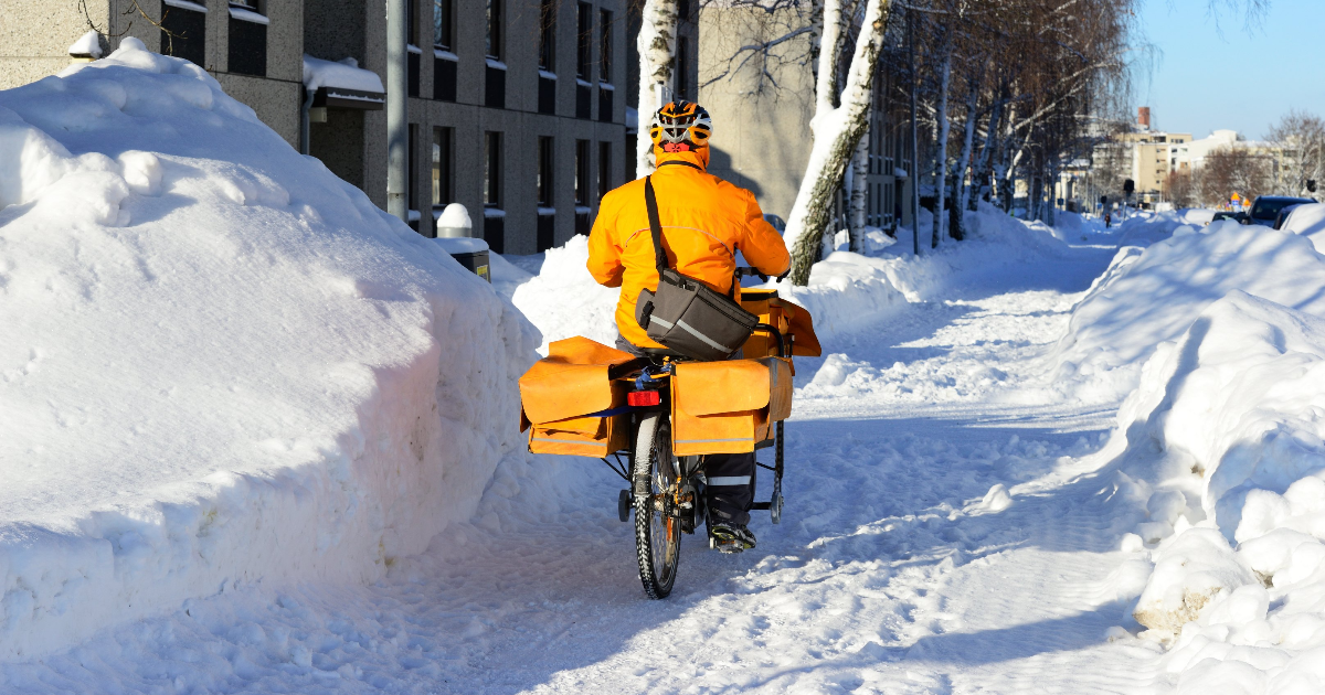Postinjakaja pyöräilee lumisella kadulla (Kuva: Shutterstock)
